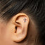 A close-up of a person's ear with a small silver key-shaped earring inserted in the earlobe.