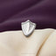 A silver metal shield-shaped object is placed on a white fabric surface against a purple background.