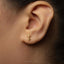 A close-up of a person's ear with a small gold key earring in the earlobe.