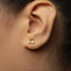 A close-up view of a person's ear wearing a small gold earring with a small car-like design.