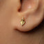 A close-up of a person's ear with a small gold earring featuring a leaf-like design.