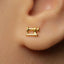 A close-up of a person's ear wearing a gold-colored earring shaped like a sewing machine.