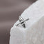 A silver earring in the shape of a canoe rests on a white surface.