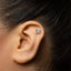 A close-up of a person's ear with a small silver sewing machine-shaped earring inserted in the earlobe.