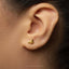 A close-up of a person's ear wearing a gold-colored earring shaped like a megaphone.