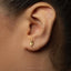 A close-up of a person's ear with a small gold earring featuring a leaf-like design.