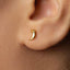 A close-up of a person's ear with a small gold earring in the earlobe.