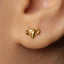 A close-up of a person's ear wearing a small gold-colored earring with a small animal-shaped charm.
