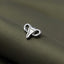 A close-up image of a silver-colored metal object, resembling a small, metallic symbol, resting on a textured fabric surface.