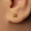 A close-up view of a person's ear with a small gold earring featuring an Om symbol.