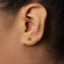 A close-up view of a person's ear with a small gold earring featuring an Om symbol.
