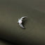 A silver crescent moon-shaped earring with a white gemstone is resting on a textured green fabric.