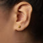 A close-up of a person's ear with a small gold earring in the earlobe.