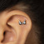 A close-up of a person's ear with a small silver earring in the shape of a heart.