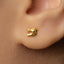 A close-up view of a person's ear, showing a small gold earring with a small design on it.