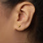 A close-up view of a person's ear, showing a small gold earring with a small design on it.