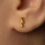 A close-up of a person's ear wearing a gold-colored earring with a small genetic code symbol on it.