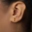 A close-up of a person's ear wearing a gold-colored earring with a small genetic code symbol on it.