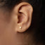 A close-up of a person's ear with a small gold cross-shaped earring in the earlobe.
