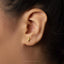 A close-up of a person's ear wearing a small gold-colored earring with a small figure on it.