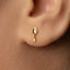 A close-up of a person's ear with a small gold earring featuring a spoon-shaped design.