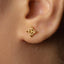 A close-up view of a person's ear with a small gold earring featuring a geometric design.