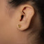 A close-up of a person's ear with a small gold earring in the earlobe.