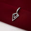 A silver-colored pendant with a triangular design is resting on a red fabric surface.