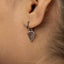 A close-up view of a person's ear adorned with a silver earring featuring a triangular design.
