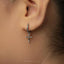 A close-up of a person's ear with a silver cross-shaped earring hanging from the earlobe.