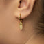 A close-up view of a person's ear wearing a gold-colored earring with a dangling charm.