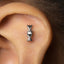 A close-up of a person's ear with a small silver earring in the shape of a DNA double helix.
