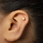 A close-up of a person's ear with a small gold-colored earring in the earlobe.