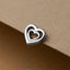 A silver heart-shaped charm or pendant is resting on a textured surface.