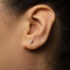 A close-up of a person's ear with a small silver earring featuring the letter "F" in the center.