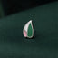 A silver pin with a green and pink leaf design rests on a dark green fabric.