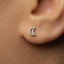 A close-up view of a person's ear with a small silver earring featuring a crescent moon design.