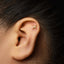 A close-up of a person's ear with a gold earring featuring a zodiac symbol in the earlobe.