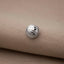 A silver basketball-shaped button is resting on a beige fabric surface.
