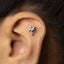 A close-up of a person's ear with a small silver earring in the shape of a palm tree.