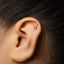 A gold earring with a Taurus symbol is visible in the ear of a person with dark hair.