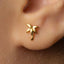 A close-up of a person's ear wearing a small gold earring shaped like a palm tree.
