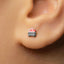 A small, silver earring with a small, red and black design is visible in the person's ear.