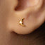 A close-up view of a person's ear with a small gold earring featuring a moon-like design.