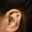A small silver earring with a small alien figure attached to the earlobe.