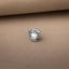 A silver-colored baseball glove pin is placed on a beige fabric surface.