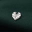 A silver heart-shaped pin is resting on a dark green fabric.