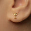 A close-up of a person's ear wearing a small gold-colored earring shaped like a martini glass.