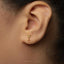 A close-up of a person's ear wearing a small gold-colored earring shaped like a martini glass.