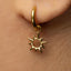 A close-up view of a person's ear wearing a gold-colored earring with a sun-shaped charm hanging from it.